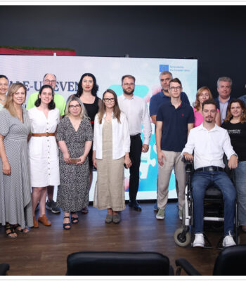 Grup de persoane la un eveniment corporativ, stând în fața unui panou de prezentare într-o cameră cu pereți roșii.